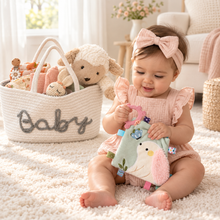 Six-month-old baby exploring a sensory cloth beside a deluxe baby girl gift basket with plush lamb.
