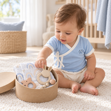 Baby wearing an Omphalodes-blue Lovingly Organics Samurai Tee while exploring a Welcome to the World baby boy gift box.